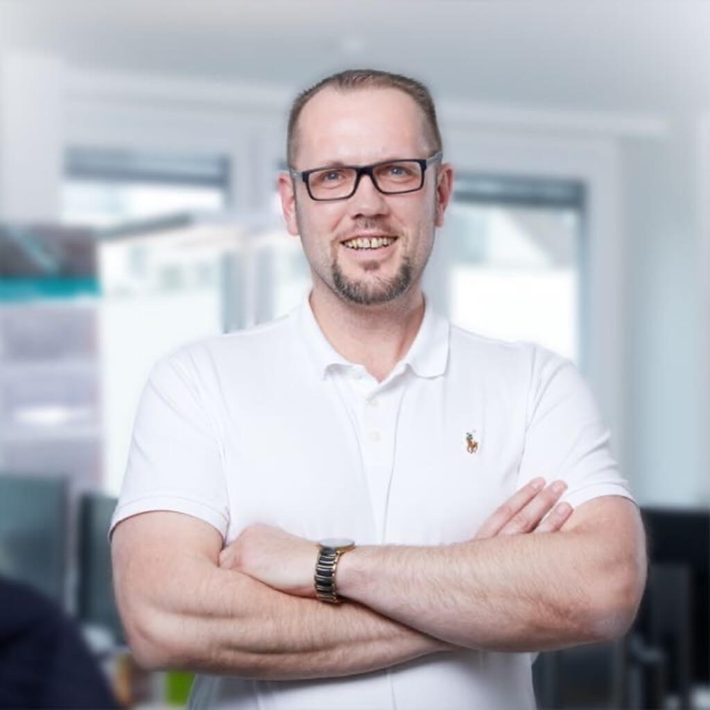 Smiling professional wearing glasses and white polo shirt with arms crossed in an office