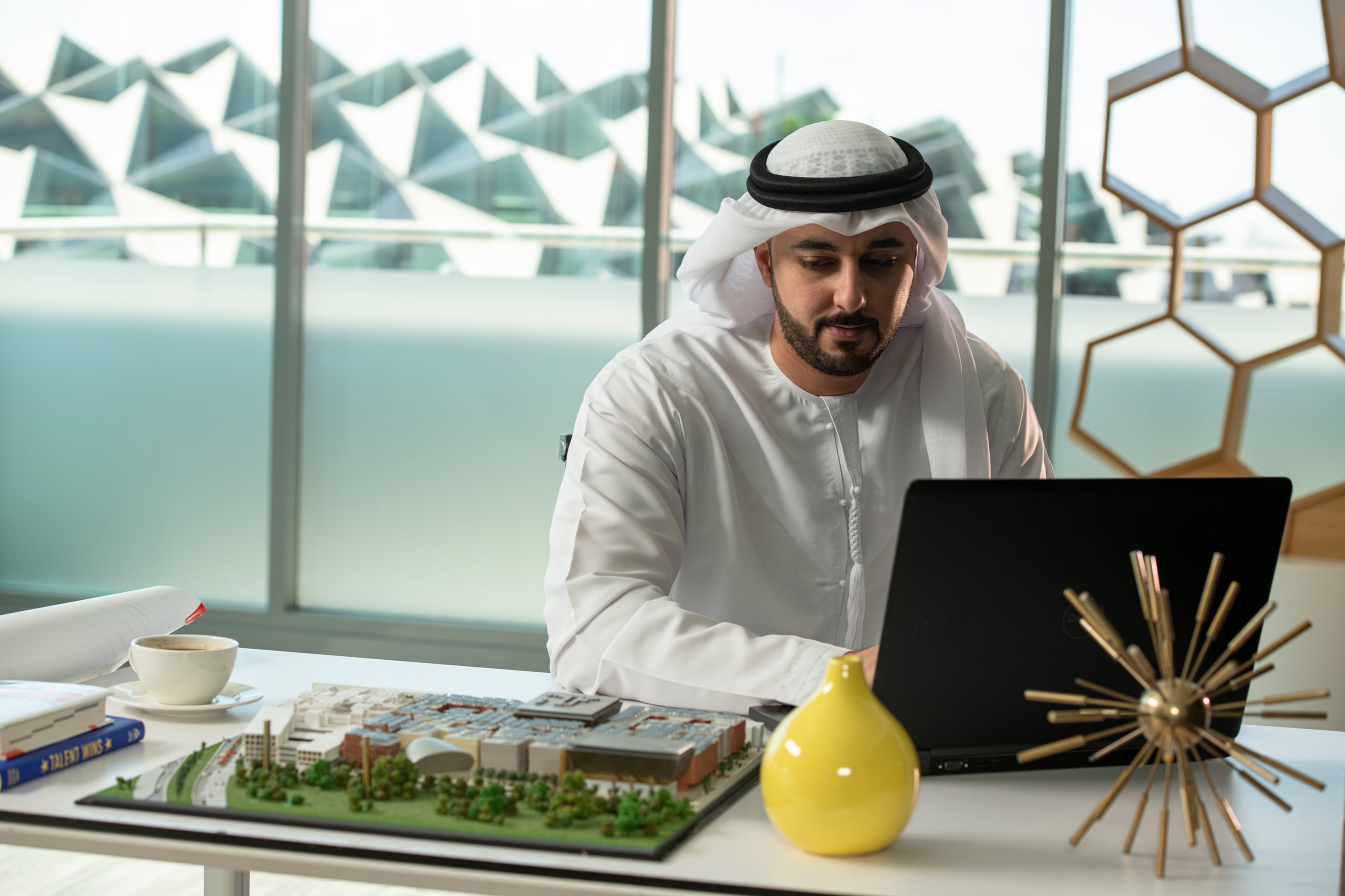 Emirati businessman working on laptop with architectural model in modern office